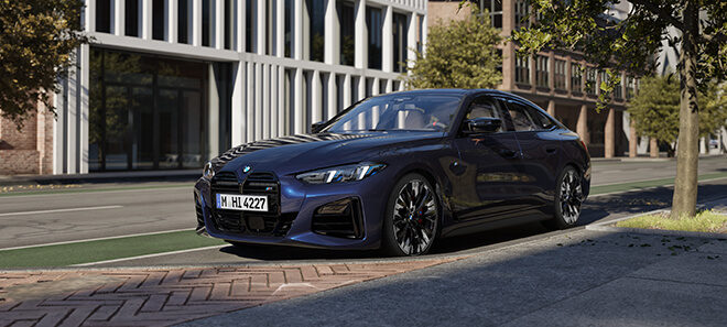 Blauer BMW 4er Gran Coupé, geparkt an einer Straße mit moderner Architektur im Hintergrund, umgeben von Bäumen und Stadtlandschaft.